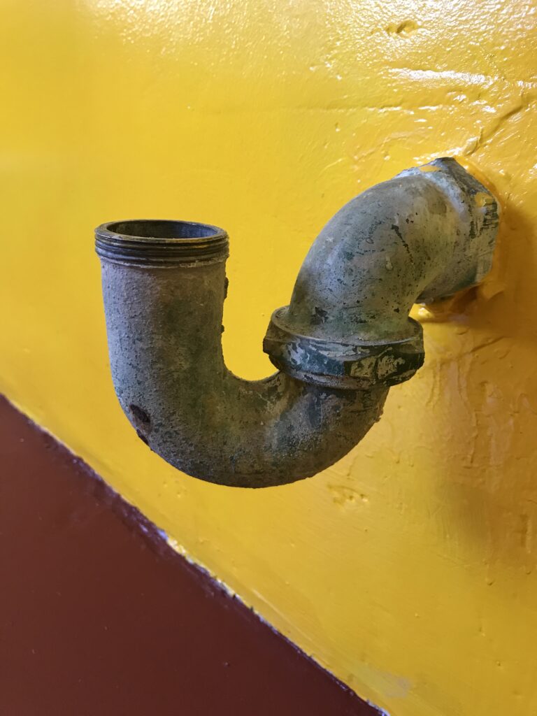 Sink gurgling troubleshooting reference: curved brass drain trap leading toward a wall drain.