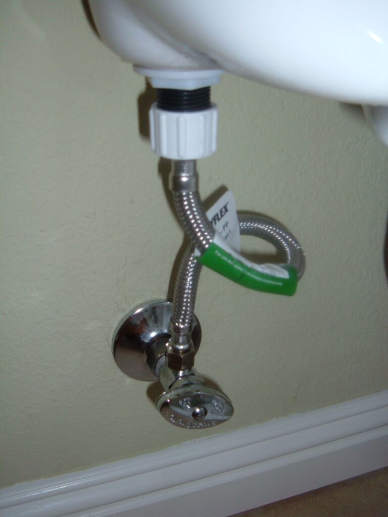 Toilet leaking at base inspection point: tank inlet coupling, braided supply hose, and wall shutoff valve.