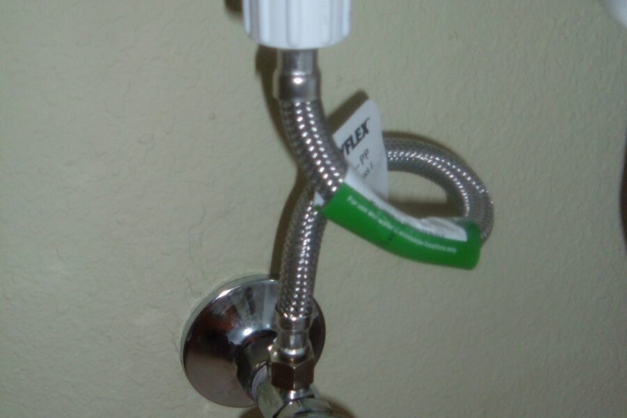 Braided toilet supply hose connecting a wall shutoff valve to the underside of the tank.