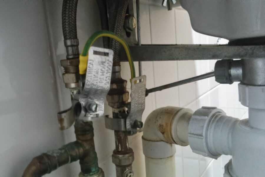 Under a sink, braided supply hoses and metal connections are visible at left, with white plastic drain joints at right.